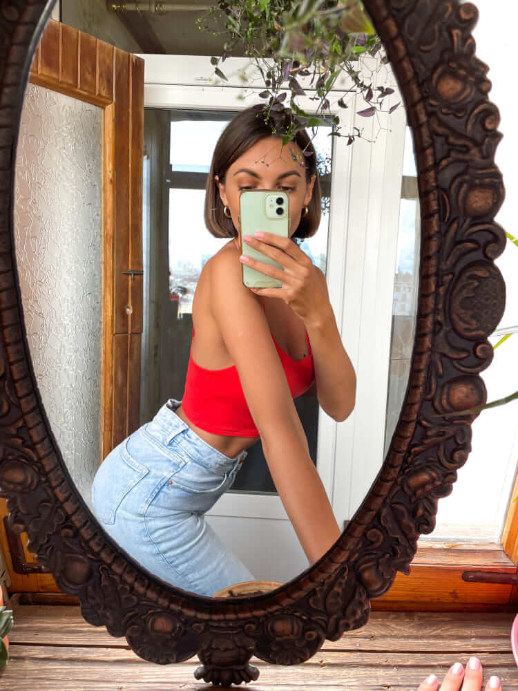A sugar baby taking a mirror selfie, wearing a red top and blue jeans